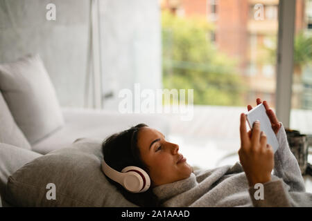 Bruna giovane donna guarda la compressa con cuffie su Foto Stock