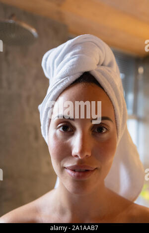 Ritratto di giovane donna bruna in un bagno con i suoi capelli avvolti in un asciugamano Foto Stock