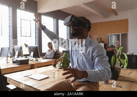 Giovani professionisti creativi uomo utilizzando cuffie VR in un ufficio soleggiato Foto Stock
