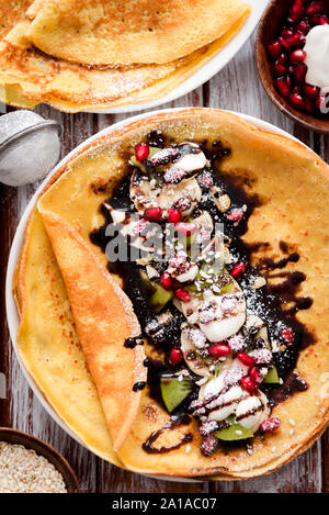 Crespelle sottili con il cioccolato fuso, i semi di sesamo, melograno e mandorle Foto Stock