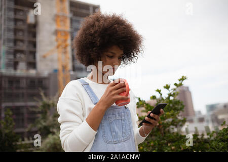 Giovane donna di bere il caffè sul balcone utilizza lo smartphone Foto Stock