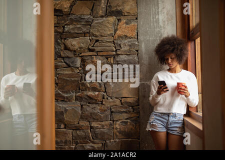 Giovane donna utilizza lo smartphone e di bere il caffè Foto Stock