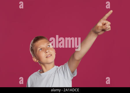 Close-up verticale di una bionda adolescente in una t-shirt bianco in posa contro una rosa di sfondo per studio. Concetto di sincere emozioni. Foto Stock