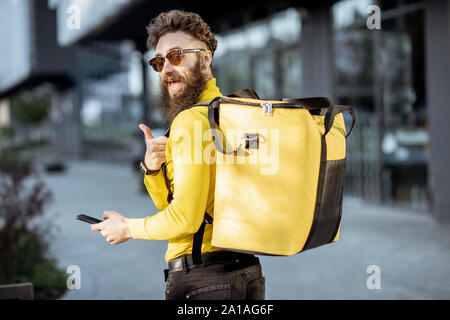 Ritratto di un allegro consegna man standing con giallo termo zaino per consegna del cibo sulla strada all'aperto Foto Stock