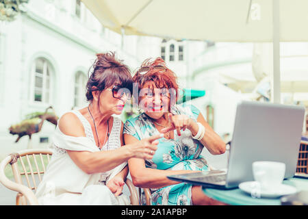 Due felici le donne anziane utilizzando laptop e puntando a schermo sorpreso mentre è seduto in outdoor cafe Foto Stock