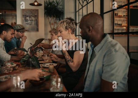 Diversi giovani amici gustando un pasto bistro di sera Foto Stock