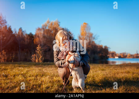 Camminare pug cane in autunno parco dal fiume. Donna Felice costeggiata pet e divertirsi con il migliore amico. Foto Stock