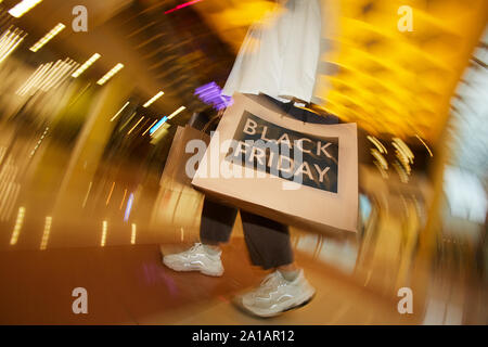 Moto offuscata della giovane donna in piedi con grande shopping bag e fare shopping nel centro commerciale Foto Stock