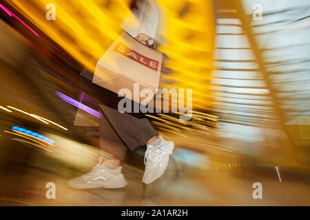 Moto offuscata della giovane donna con carta shopping bags facendo shopping durante la vendita nel negozio Foto Stock