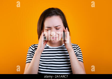 Stanco bruna giovane razza mista donna mantiene le mani sulle tempie, chiude eyeson sfondo giallo Foto Stock