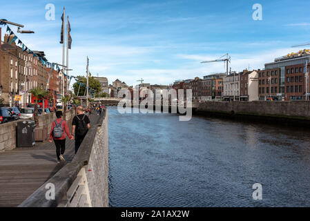 La gente che camminava sul fiume Liffey Boardwalk con il Millennio e Ha'penny ponti in background in Dublino, Irlanda Foto Stock
