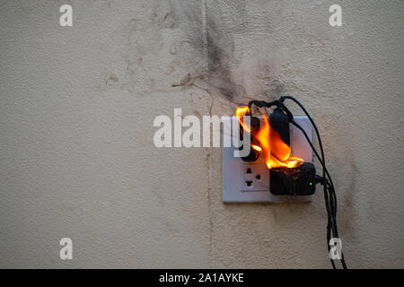 Sul fuoco un adattatore a spina femmina su sfondo bianco, corto circuito elettrico a guasto derivante in elettricità filo bruciato Foto Stock