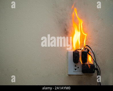 Sul fuoco un adattatore a spina femmina su sfondo bianco, corto circuito elettrico a guasto derivante in elettricità filo bruciato Foto Stock