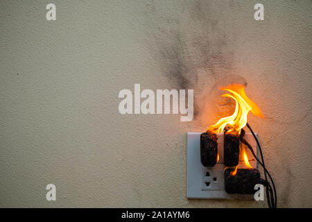 Sul fuoco un adattatore a spina femmina su sfondo bianco, corto circuito elettrico a guasto derivante in elettricità filo bruciato Foto Stock