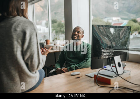 Sorridente African American designer nel corso di una conversazione con un collega di lavoro Foto Stock