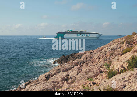 Ibiza, Spagna - Luglio 03, 2019: spiaggia rocciosa e un traghetto veloce Foto Stock