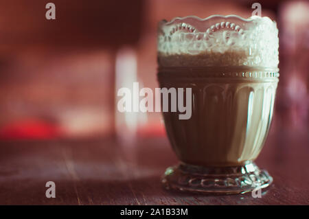 Caffè Latte in una insolita di vetro con i modelli antichi. American in utensili antichi su una superficie strutturata tavolo in legno, stile vintage e tonificante morbido. Concep Foto Stock