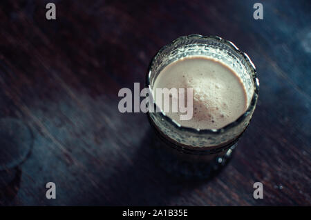 Caffè Latte in una insolita di vetro con i modelli antichi. American in utensili antichi su una superficie strutturata tavolo in legno, stile vintage e tonificante morbido. Copia s Foto Stock