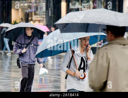 Belgrado, Serbia- Settembre 24, 2018: giovane donna che cammina di fretta sotto un ombrello mentre a parlare su un telefono mobile in una piovosa e la folla via della città Foto Stock