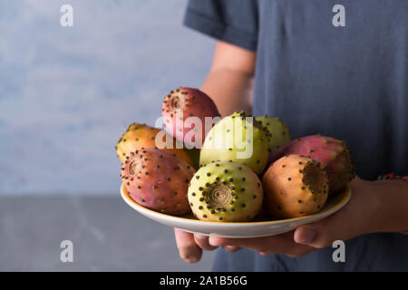 Mani femminili tenere una piastra con maturi frutti freschi di ficodindia su sfondo grigio, copia dello spazio. L' Opuntia frutta crescere in Puglia, Italia Foto Stock