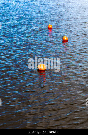 Tre arancio brillante Boe galleggiante sul fiume della superficie dell'acqua. Set di tre di sicurezza arancione boe in un fiume con piccole onde sulla superficie dell'acqua. Foto Stock