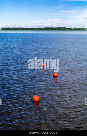 Tre arancio brillante Boe galleggiante sul fiume di acqua superficiale con bosco all'orizzonte. Set di tre arancione boe di sicurezza lo stiramento nella distanza. Foto Stock