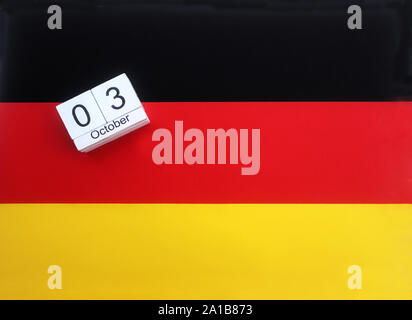 Cubi di legno con la data del giorno dell'unità tedesca, 3 ottobre, giacente su una bandiera tedesca Foto Stock