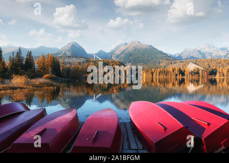Il pittoresco paesaggio autunnale con fila di rosso le barche in legno e le alte montagne sullo sfondo. Il villaggio di Strbske Pleso lago in Alti Tatra National Park, Slovacchia Foto Stock