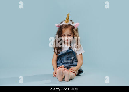 Bambina indossa la fascia di unicorn, seduto sul pavimento su sfondo blu Foto Stock