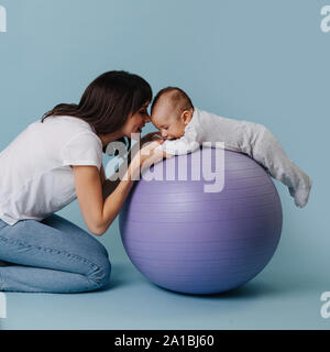 Felice madre facendo esercizi con il suo neonato Bambino su viola la sfera di yoga Foto Stock