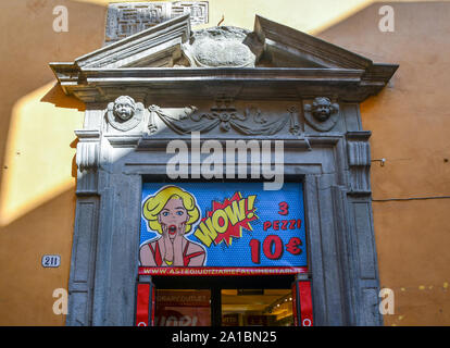 Close-up di un antico casale in pietra del telaio della porta e il timpano con un negozio accedi pop art stile nel centro storico di Lucca, Toscana, Italia Foto Stock