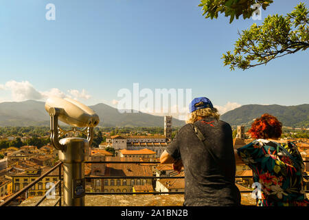 Vista panoramica del centro della città di Lucca dalla Torre Guinigi con un paio di turisti da dietro e un binocolo in estate, Toscana, Italia Foto Stock