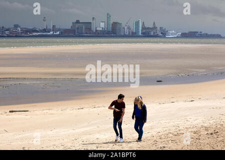 New Brighton beach promenade, Wallasey. una coppia giovane camminando lungo la sabbia con Liverpool skyline dietro Foto Stock