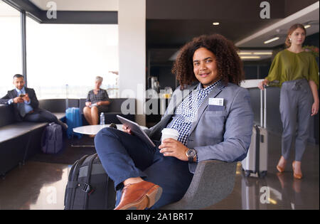 African American uomo in attesa per il volo seduti in aeroporto moderno lounge su tablet con bagagli Foto Stock