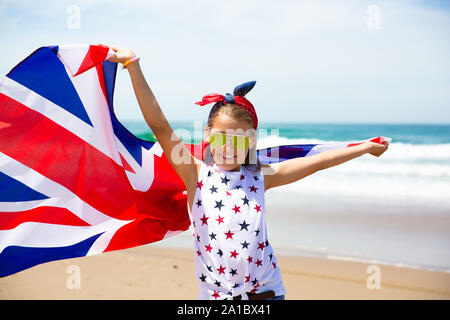 Felice ragazza britannico porta svolazzanti Blu Bianco Rosso bandiera della Gran Bretagna, del Regno Unito e Irlanda del Nord contro il cielo blu e l'oceano indietro Foto Stock