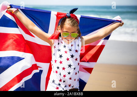 Felice ragazza britannico porta svolazzanti Blu Bianco Rosso bandiera della Gran Bretagna, del Regno Unito e Irlanda del Nord contro il cielo blu e l'oceano indietro Foto Stock