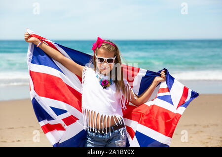 Felice ragazza britannico porta svolazzanti Blu Bianco Rosso bandiera della Gran Bretagna, del Regno Unito e Irlanda del Nord contro il cielo blu e l'oceano indietro Foto Stock
