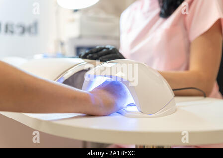La donna nel salone di bellezza. La donna trattiene il manicure fresca nell'UV LED lampada per unghie. Processo di essiccamento del gel sui chiodi, vicino. La bellezza e la cura di sé. Foto Stock