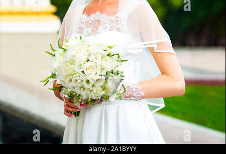 La sposa in un bellissimo abito bianco tiene nelle sue mani un bel mazzo di nozze. Lussuoso sposa il bouquet di rose bianche e eustomas. La squisita Foto Stock