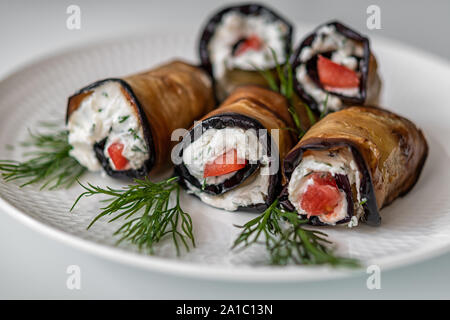 Involtini di melanzane con formaggio e pomodoro con aneto rami su una piastra bianca su sfondo bianco Foto Stock