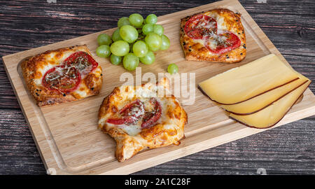 Torta fatta in casa con pomodoro e formaggio giacciono su una tavola di legno accanto all'uva e pezzi di formaggio Foto Stock