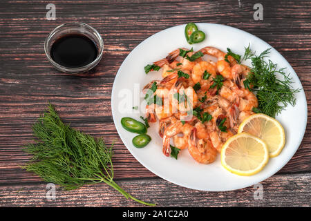Gamberi fritti in salsa alla panna con un piatto sul tavolo con il limone ed aneto, accanto a rami di aneto e salsa di soia Foto Stock
