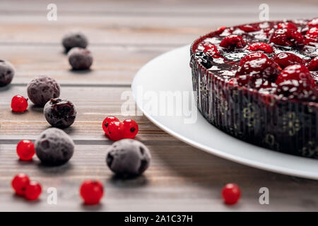Torta con frutti di bosco: lampone, ribes, fragole su una piastra bianca su uno sfondo di legno, nei pressi di ribes rosso e ciliegia Foto Stock
