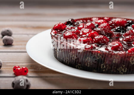 Torta con bacche di close-up: lampone, ribes, fragole su una piastra bianca su uno sfondo di legno, nei pressi di ribes rosso e ciliegia Foto Stock