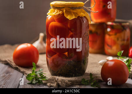 In casa di vasetti di pomodori marinati su un rustico sfondo di legno. Decapati e conserve di prodotto. Accanto i pomodori e altri per la cottura. Foto Stock