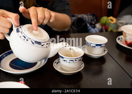 Teiera nelle mani di una ragazza versando il tè verde in belle coppe cinese Foto Stock