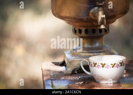 Vintage samovar bronzo la combustione del legno e la coppa sul tavolo arrugginita all'aperto, la preparazione di acqua per il tè di birra, il fuoco selettivo Foto Stock