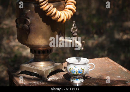 Vintage samovar bronzo la combustione del legno e la coppa sul tavolo arrugginita all'aperto, la preparazione di acqua per il tè di birra, il fuoco selettivo Foto Stock