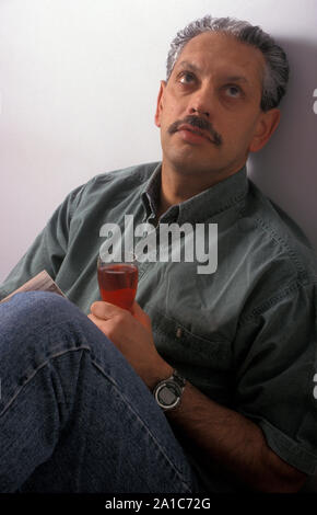 Infelice indiano maturo uomo seduto con un bicchiere di vino rosso Foto Stock