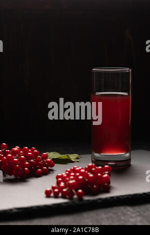 Succo rosso da pallon di maggio in un vetro su uno sfondo nero. Nei pressi di viburnum bacche.il cibo sano Foto Stock